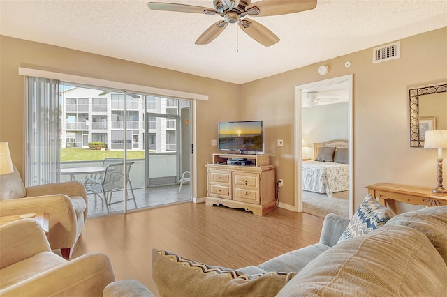 living room with light hardwood / wood-style flooring, a textured ceiling, and ceiling fan