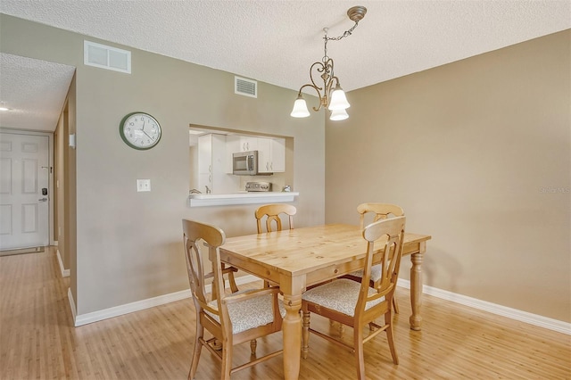 dining room with a textured ceiling, an inviting chandelier, and light wood-type flooring