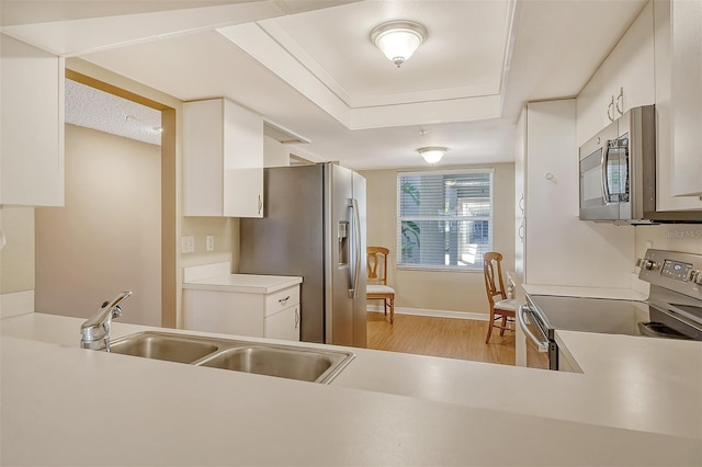 kitchen featuring white cabinets, a raised ceiling, appliances with stainless steel finishes, light hardwood / wood-style floors, and sink