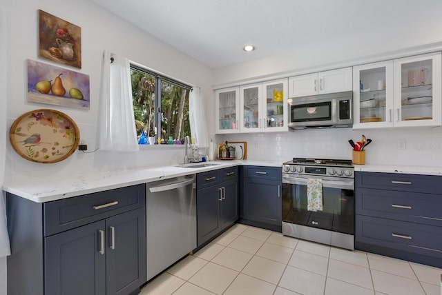 kitchen with sink, appliances with stainless steel finishes, light tile patterned floors, backsplash, and white cabinets