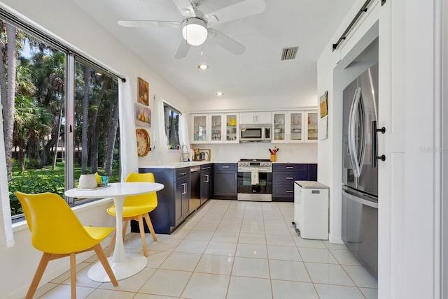 kitchen with white cabinets, appliances with stainless steel finishes, a barn door, and light tile patterned flooring