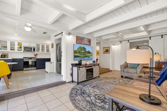 tiled living room with a barn door, ceiling fan, and beam ceiling