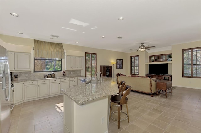 kitchen featuring a wealth of natural light, an island with sink, backsplash, and ceiling fan