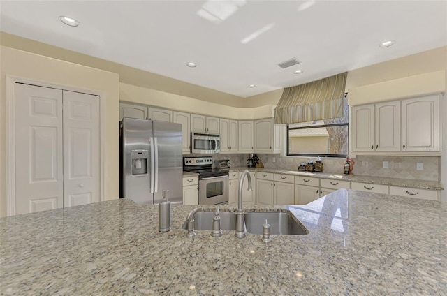 kitchen with sink, light stone countertops, stainless steel appliances, and backsplash