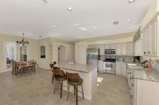 kitchen featuring appliances with stainless steel finishes, light stone countertops, and a center island with sink