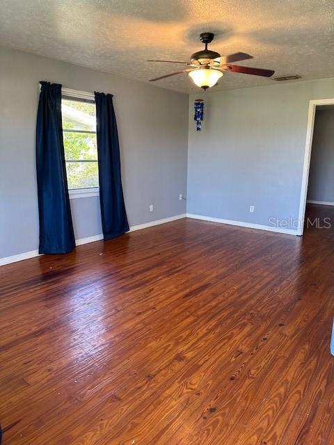 empty room featuring a textured ceiling, dark wood-type flooring, and ceiling fan