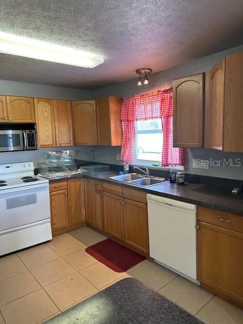 kitchen with sink, light tile patterned flooring, a textured ceiling, and white appliances