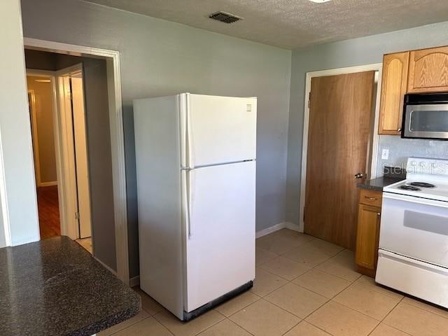 kitchen featuring a textured ceiling, light tile patterned floors, and white appliances