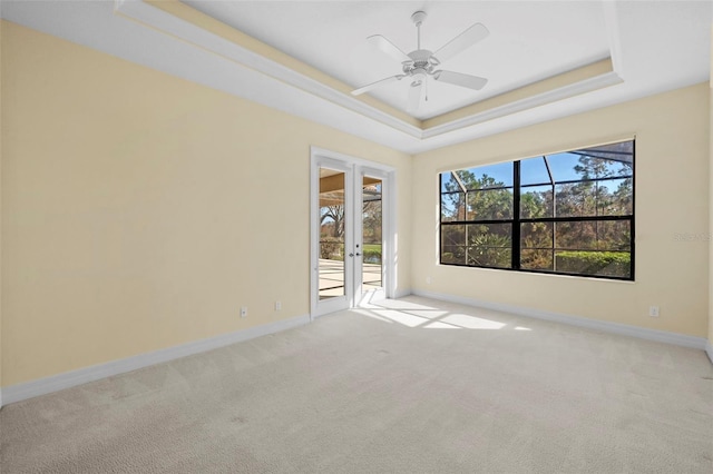 empty room featuring light carpet, a raised ceiling, and ceiling fan