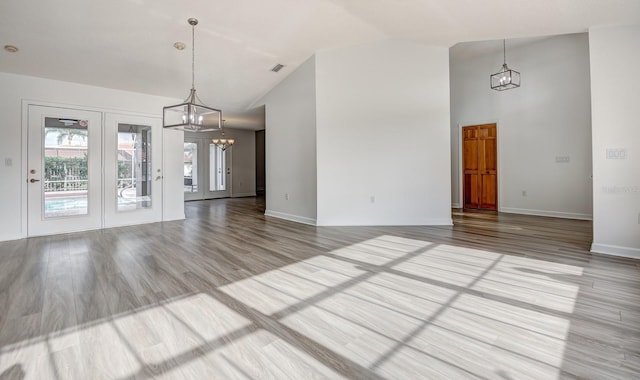 unfurnished dining area featuring high vaulted ceiling, light wood-style flooring, visible vents, baseboards, and an inviting chandelier