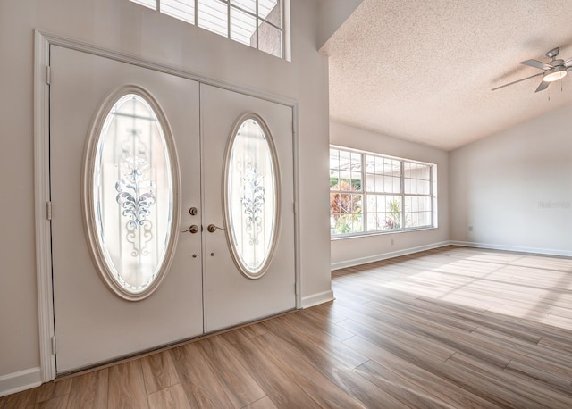 entryway with lofted ceiling, light wood-style flooring, ceiling fan, a textured ceiling, and french doors