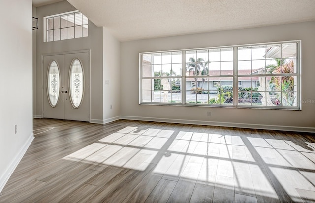 foyer featuring french doors, a textured ceiling, baseboards, and wood finished floors