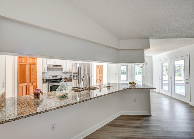 kitchen with light stone counters, a peninsula, stainless steel appliances, a sink, and white cabinetry