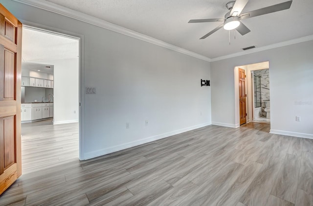 spare room featuring light wood-style flooring, visible vents, baseboards, a ceiling fan, and ornamental molding