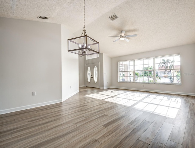 unfurnished living room featuring a textured ceiling, wood finished floors, visible vents, and baseboards