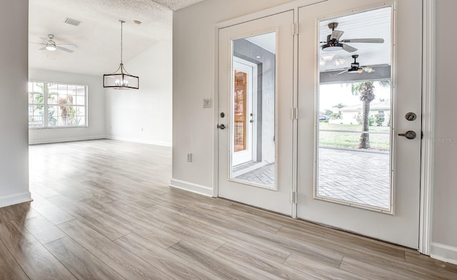 doorway to outside featuring light wood-type flooring, baseboards, a textured ceiling, and ceiling fan with notable chandelier