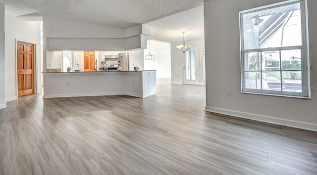 unfurnished living room featuring baseboards, vaulted ceiling, a textured ceiling, light wood-style floors, and a chandelier