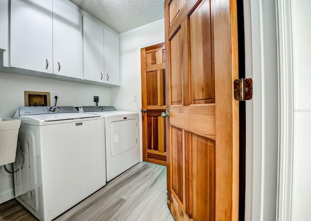 washroom with light wood-style floors, cabinet space, a textured ceiling, and washer and clothes dryer