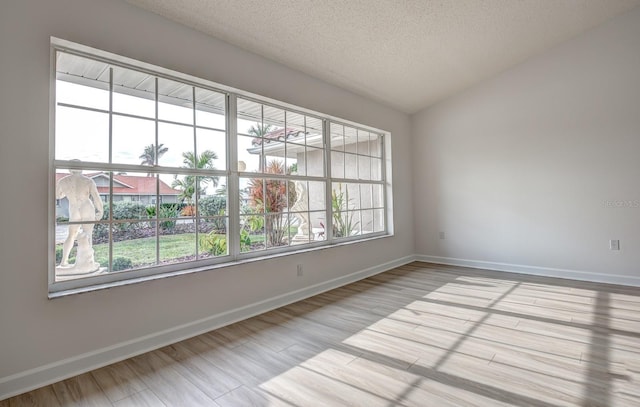 spare room with lofted ceiling, light wood finished floors, baseboards, and a textured ceiling