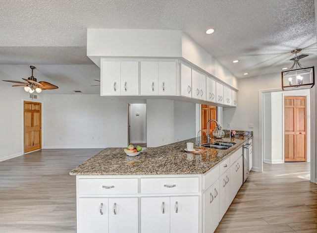 kitchen with light wood-type flooring, dark stone counters, white cabinets, and dishwasher