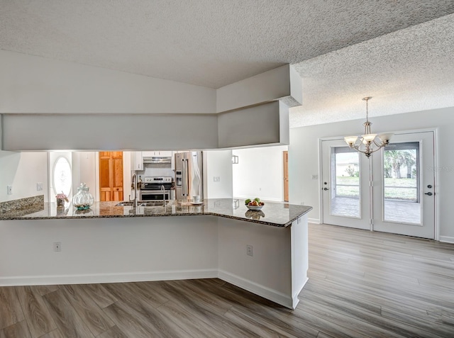 kitchen featuring a peninsula, stainless steel appliances, hanging light fixtures, light wood-type flooring, and dark stone countertops