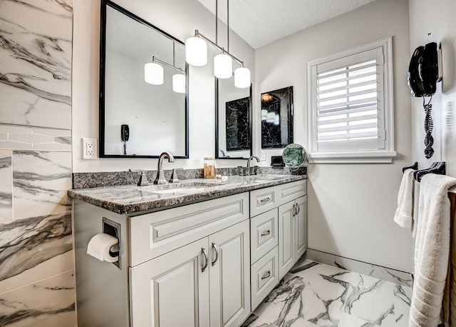 bathroom featuring marble finish floor, a sink, a textured ceiling, and double vanity