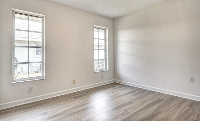 unfurnished room with light wood-style flooring, baseboards, and a textured ceiling