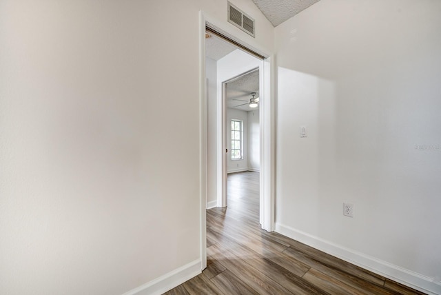 hall featuring a textured ceiling, wood finished floors, visible vents, and baseboards