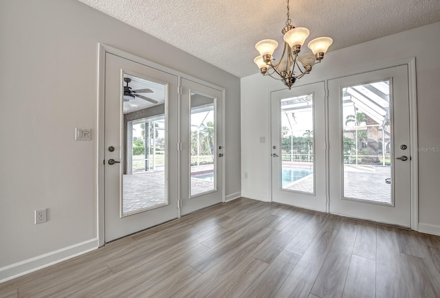 doorway featuring light wood-style floors, baseboards, a chandelier, and a textured ceiling