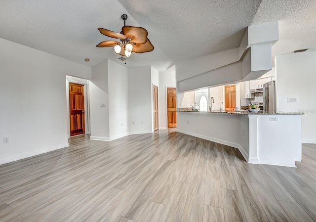 unfurnished living room with baseboards, visible vents, a ceiling fan, a textured ceiling, and light wood-style floors