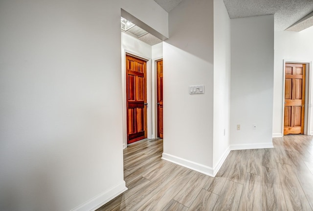 corridor with light wood-type flooring, a textured ceiling, and baseboards