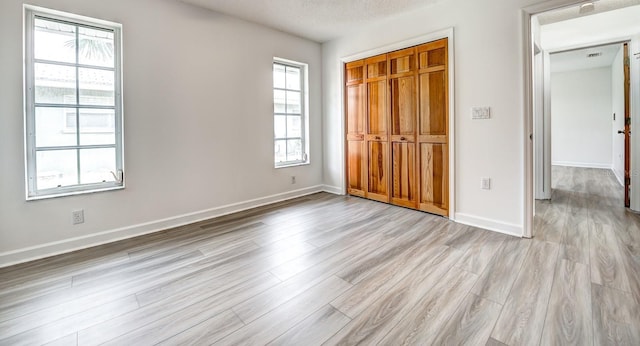 unfurnished bedroom with light wood-style floors, a closet, a textured ceiling, and baseboards