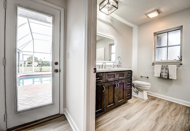 half bathroom featuring a textured ceiling, toilet, wood finished floors, and vanity