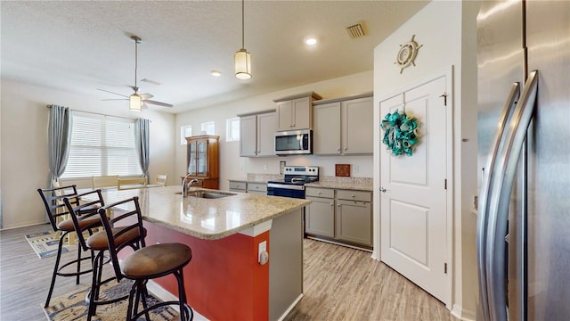 kitchen featuring a center island with sink, appliances with stainless steel finishes, a kitchen bar, light hardwood / wood-style flooring, and gray cabinetry