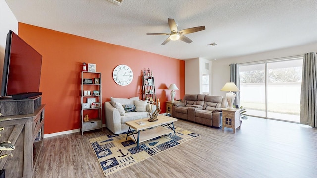 living room with a textured ceiling, wood-type flooring, and ceiling fan