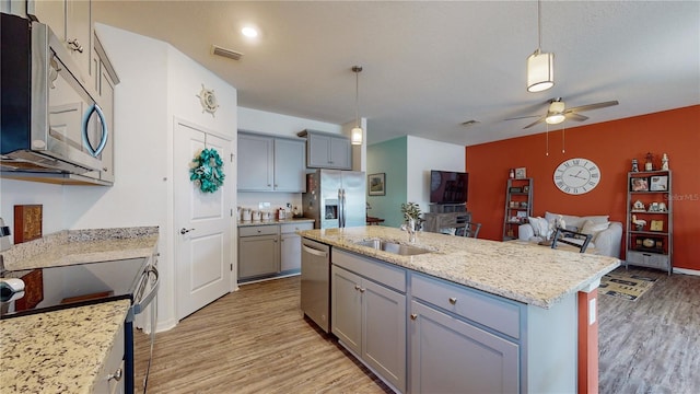 kitchen featuring a kitchen island with sink, stainless steel appliances, sink, pendant lighting, and light wood-type flooring