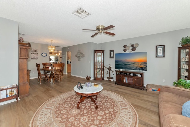 living room with a textured ceiling, ceiling fan with notable chandelier, and light wood-type flooring