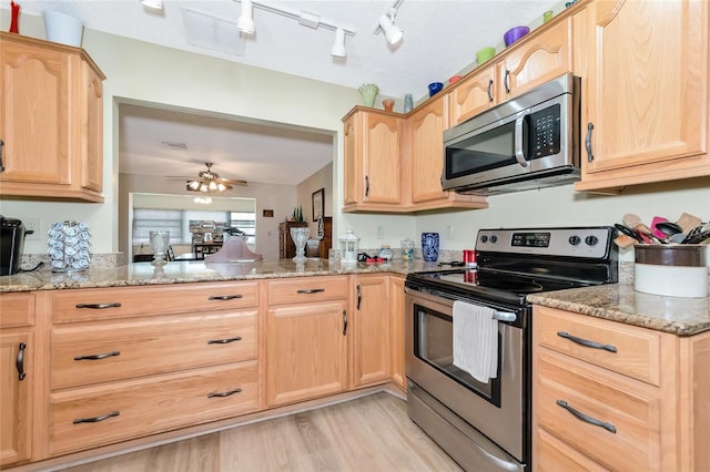 kitchen with ceiling fan, light stone counters, stainless steel appliances, and kitchen peninsula