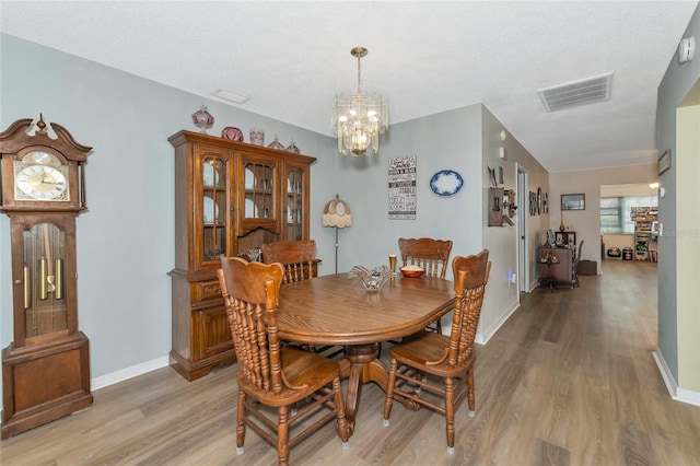 dining area with a textured ceiling, light hardwood / wood-style flooring, and a chandelier