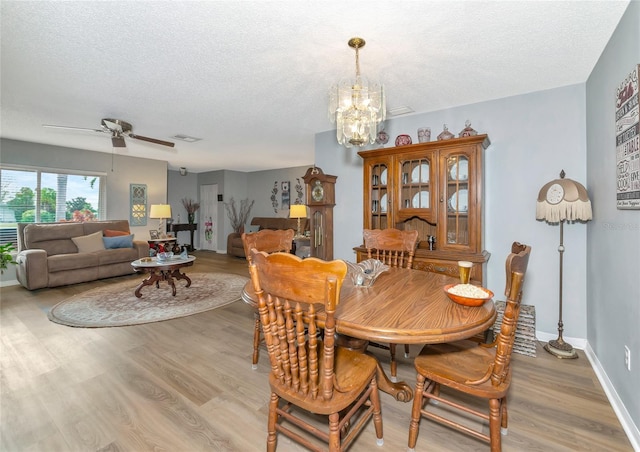 dining area with light hardwood / wood-style floors, a textured ceiling, and ceiling fan with notable chandelier