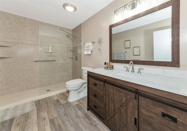 bathroom featuring toilet, hardwood / wood-style flooring, vanity, and a tile shower