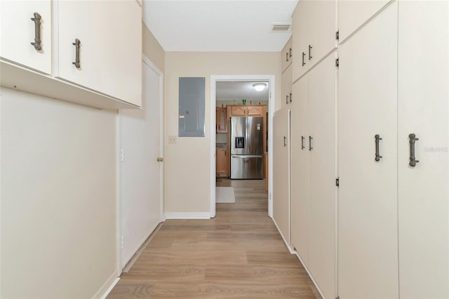 hallway with light hardwood / wood-style flooring, a textured ceiling, and electric panel