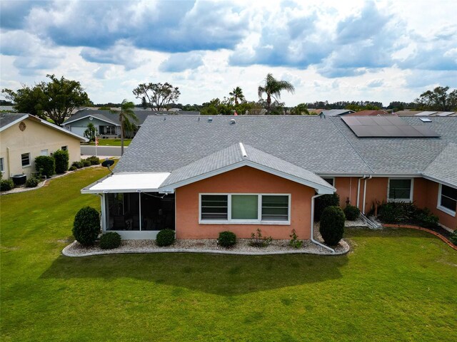 back of house with a yard, a sunroom, and solar panels