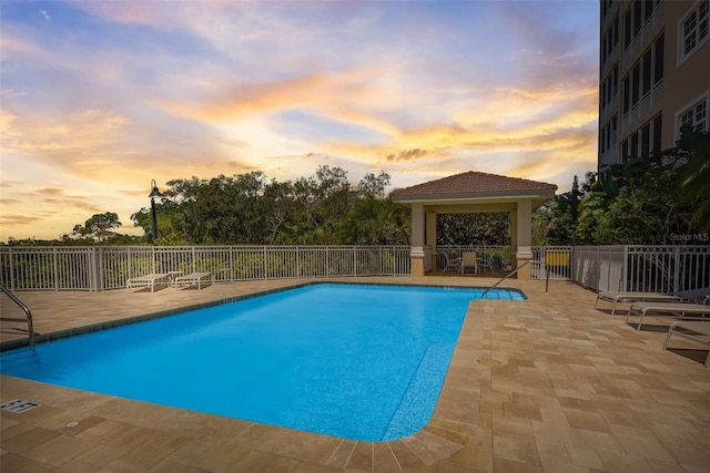 pool at dusk with a gazebo and a patio area