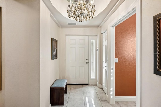 tiled foyer with a tray ceiling, ornamental molding, and an inviting chandelier