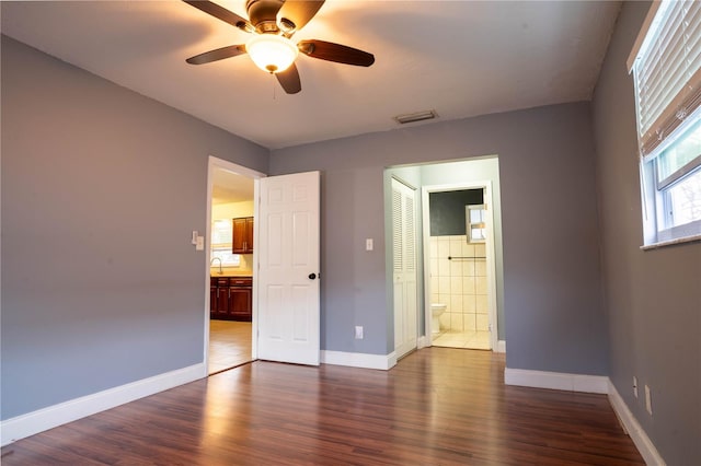 unfurnished bedroom with ensuite bathroom, ceiling fan, a closet, and dark hardwood / wood-style flooring