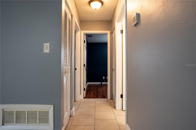 hallway with a textured ceiling and light tile patterned floors