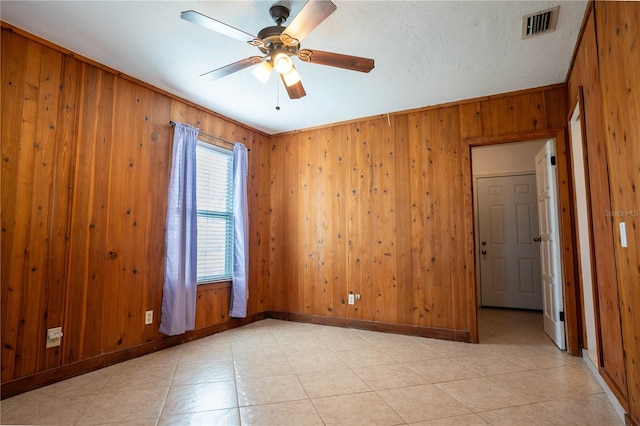 empty room featuring a textured ceiling, wood walls, ceiling fan, and crown molding