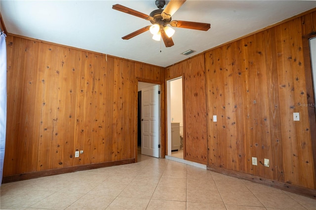 spare room featuring crown molding, wooden walls, ceiling fan, and light tile patterned floors