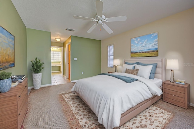 carpeted bedroom featuring multiple windows, a textured ceiling, ceiling fan, and ensuite bathroom